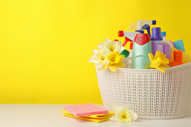 Plastic basket with spring flowers and cleaning supplies on wooden table. Space for text