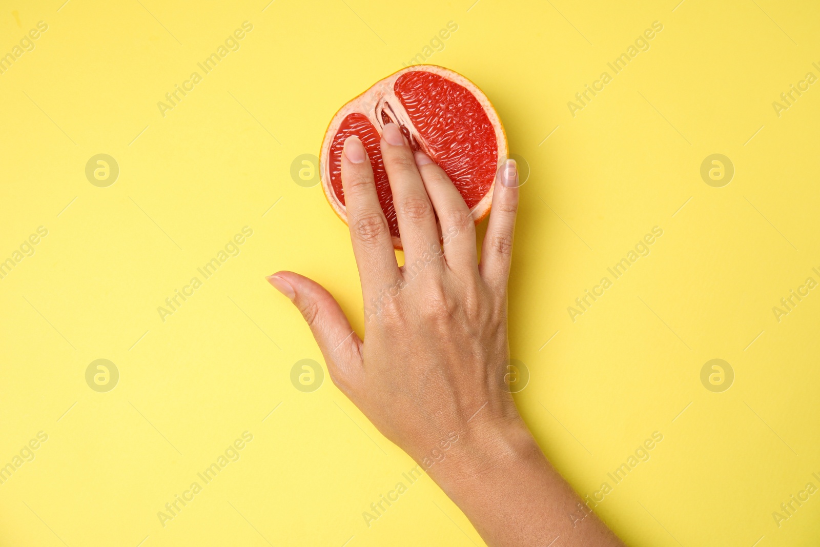 Photo of Young woman touching half of grapefruit on yellow background, top view. Sex concept