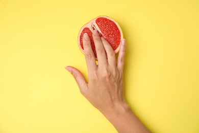 Young woman touching half of grapefruit on yellow background, top view. Sex concept