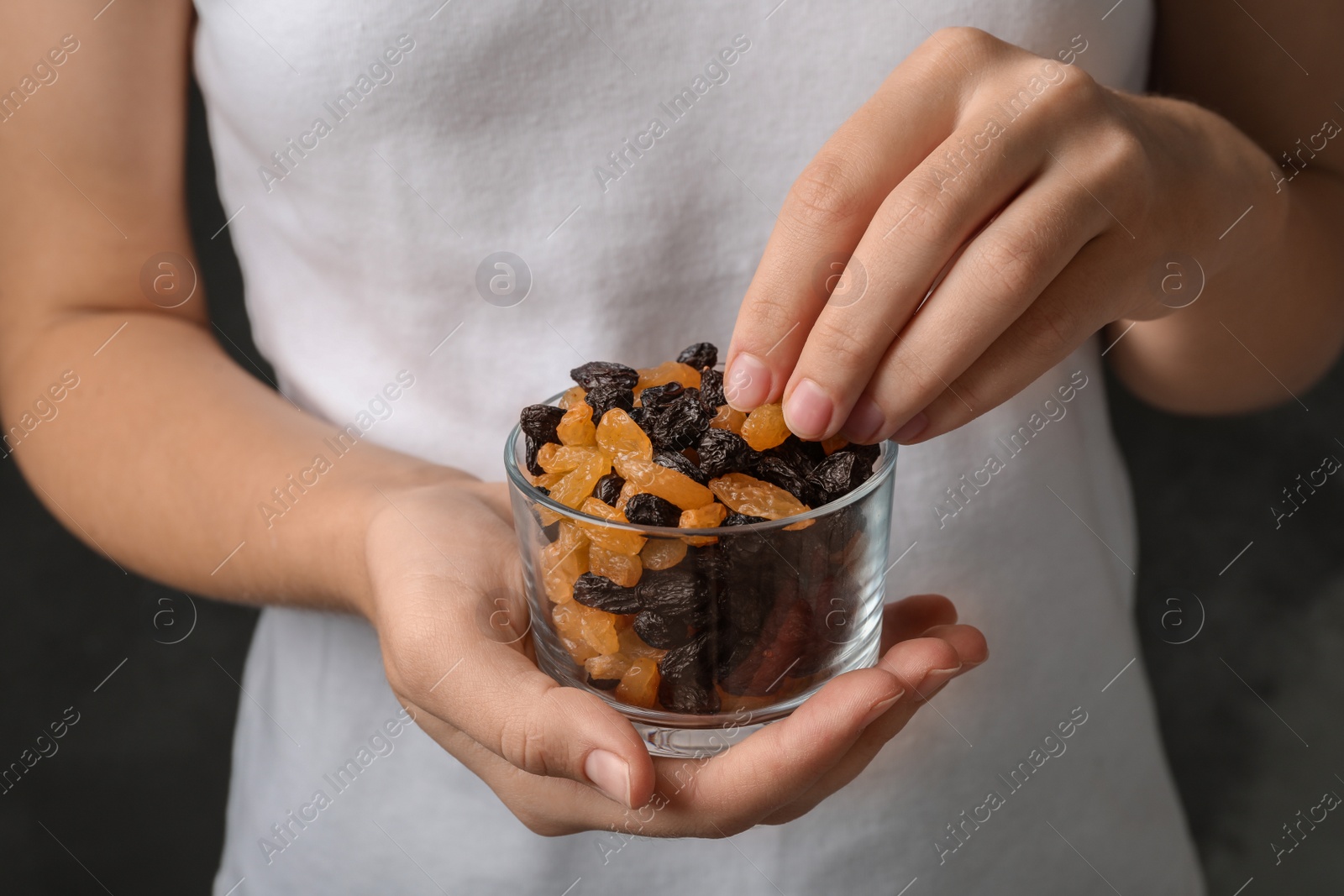 Photo of Woman holding glass with raisins on black background, closeup