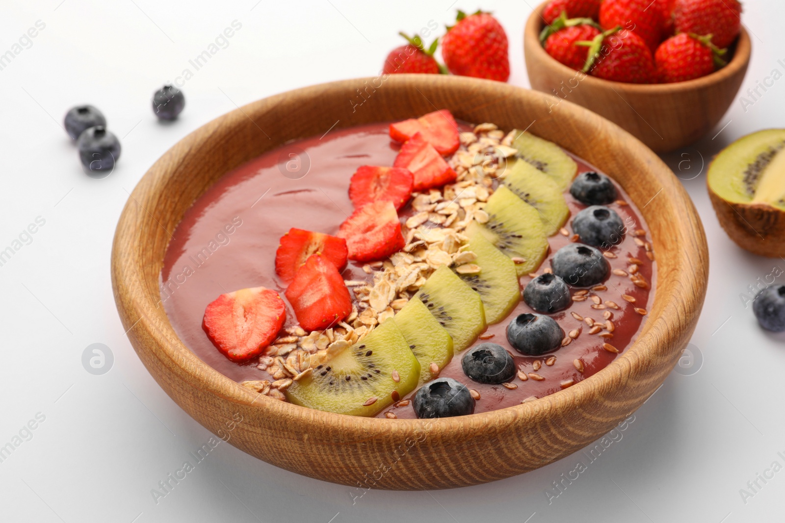 Photo of Bowl of delicious smoothie with fresh blueberries, strawberries, kiwi slices and oatmeal on white background