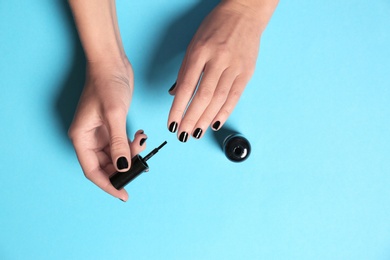 Photo of Woman applying nail polish with brush on color background, top view