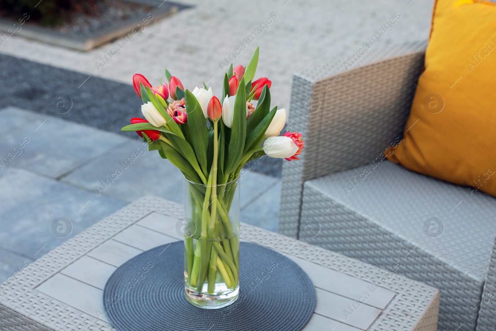 Photo of Beautiful bouquet of colorful tulips on rattan garden table outdoors