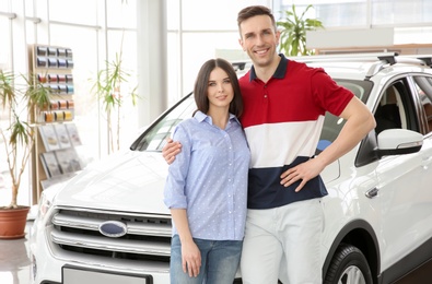 Young couple near auto in salon. Buying new car