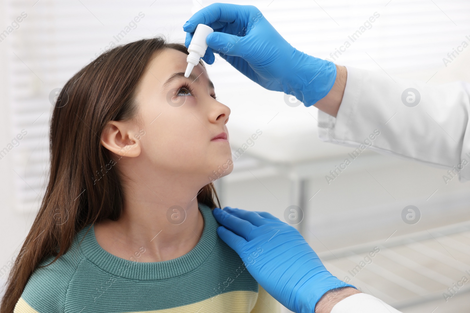 Photo of Doctor applying medical drops into girl's eye indoors