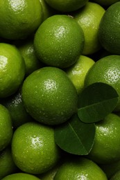 Photo of Fresh ripe limes and leaves with water drops as background, top view