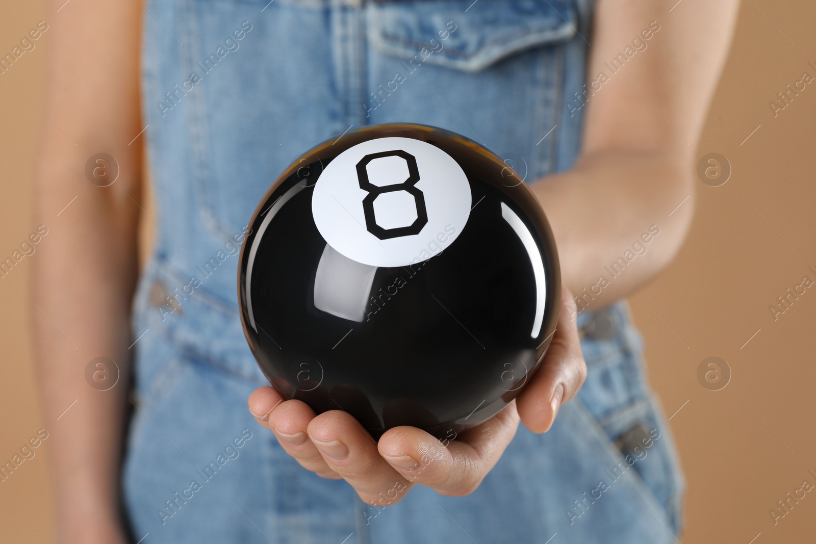 Photo of Woman holding magic eight ball on light brown background, closeup