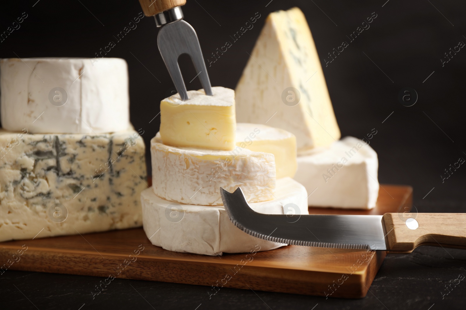 Photo of Different types of cheese, knife and fork on black table, closeup