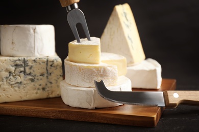 Photo of Different types of cheese, knife and fork on black table, closeup