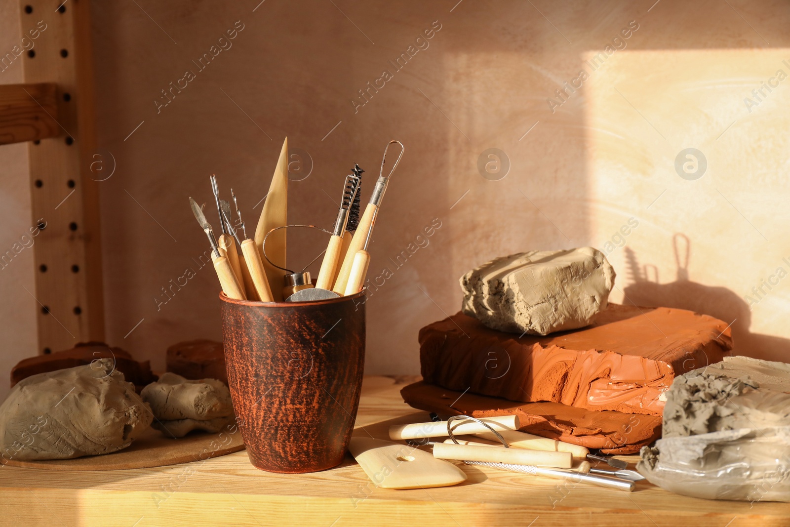 Photo of Clay and set of modeling tools on wooden table in workshop