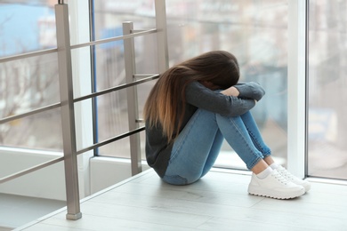 Photo of Upset teenage girl sitting at window indoors