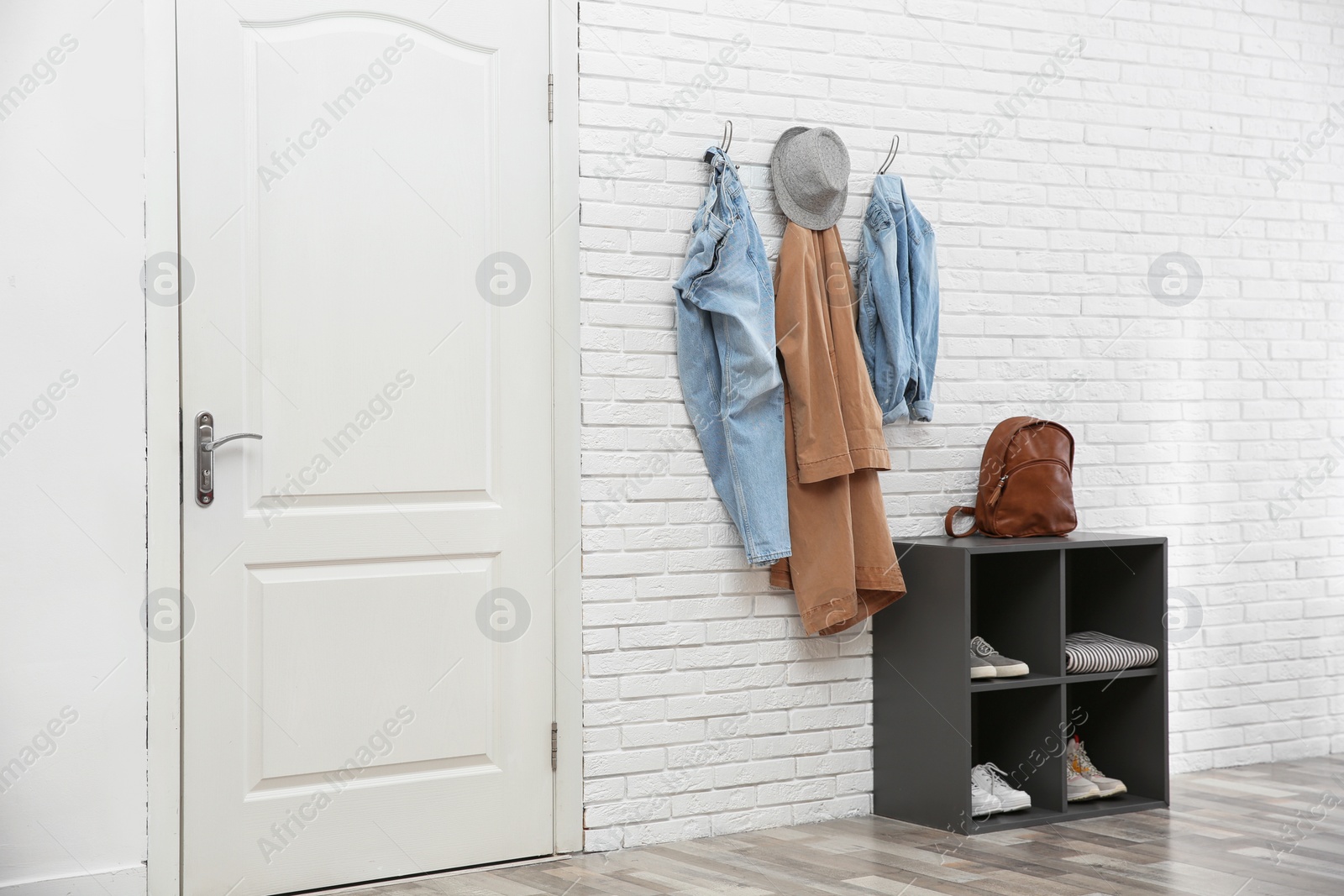 Photo of Stylish hallway interior with door, shoe rack and clothes hanging on brick wall