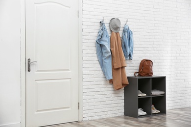 Photo of Stylish hallway interior with door, shoe rack and clothes hanging on brick wall