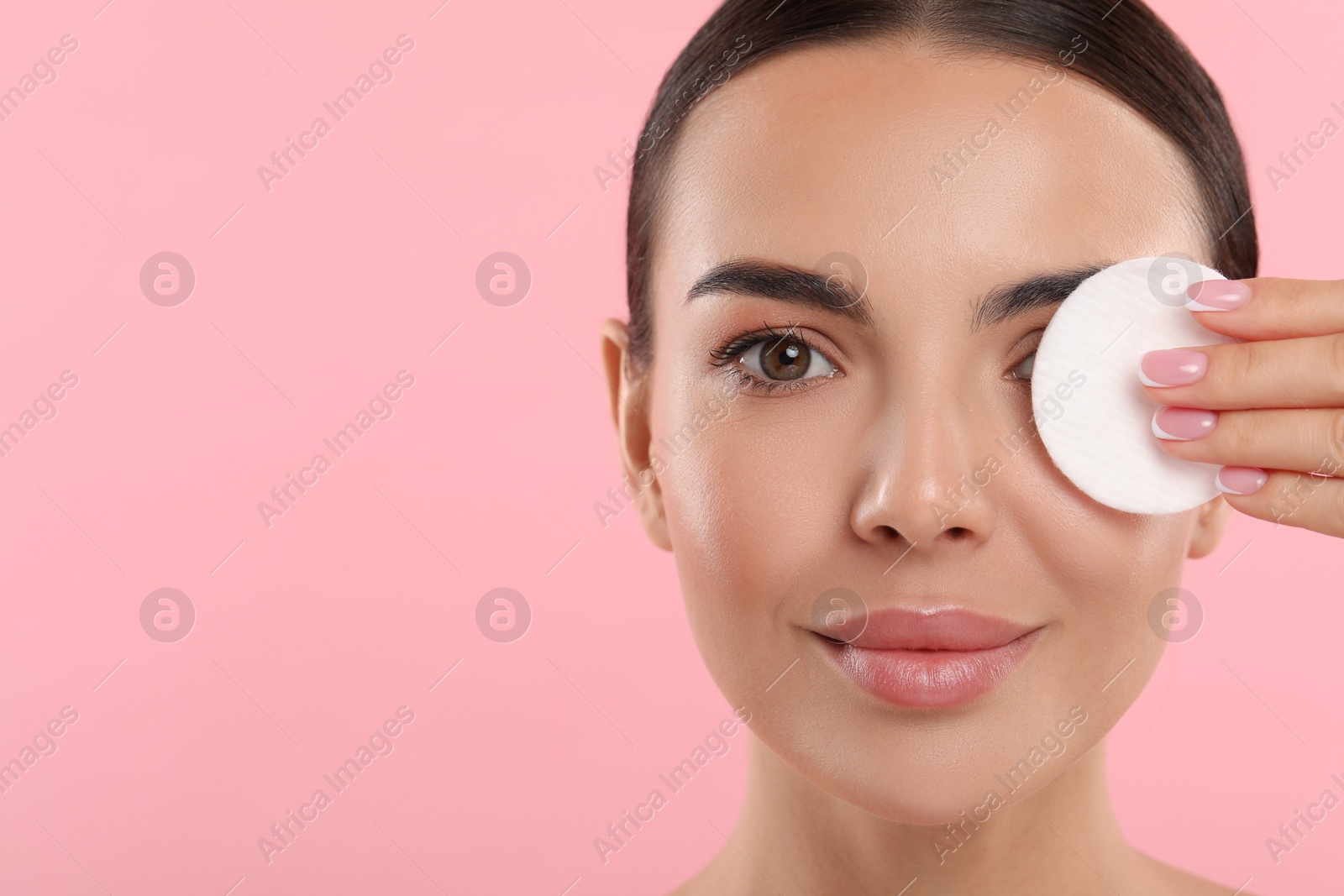 Photo of Beautiful woman removing makeup with cotton pad on pink background, closeup. Space for text