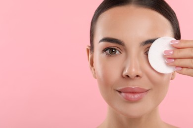 Photo of Beautiful woman removing makeup with cotton pad on pink background, closeup. Space for text