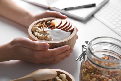 Woman with tasty granola at workplace, closeup