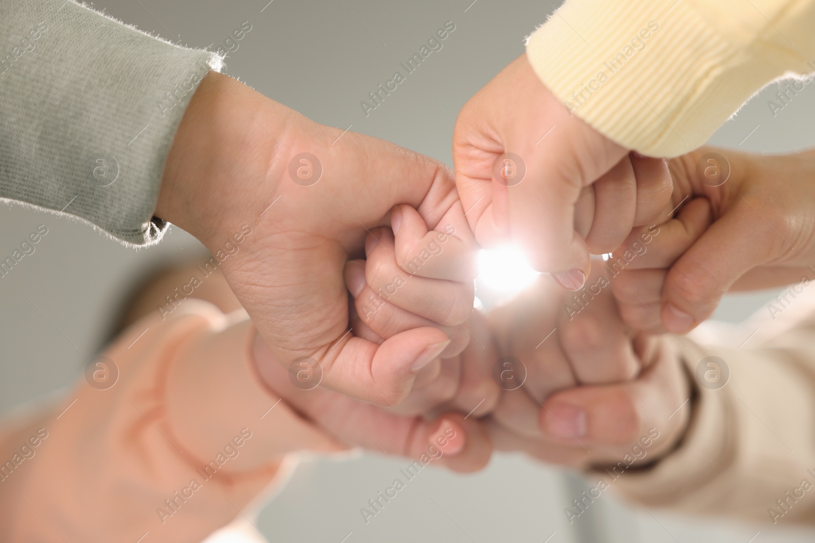 Photo of Group of people holding fists together indoors, low angle view. Unity concept