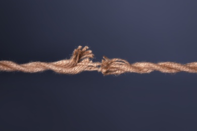 Photo of Stretched frayed rope breaking on dark background