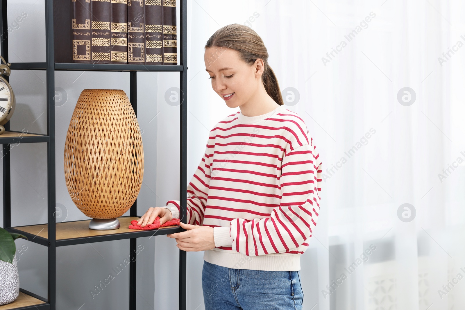 Photo of Woman cleaning shelving unit with rag at home