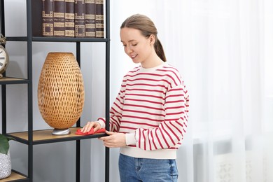 Photo of Woman cleaning shelving unit with rag at home