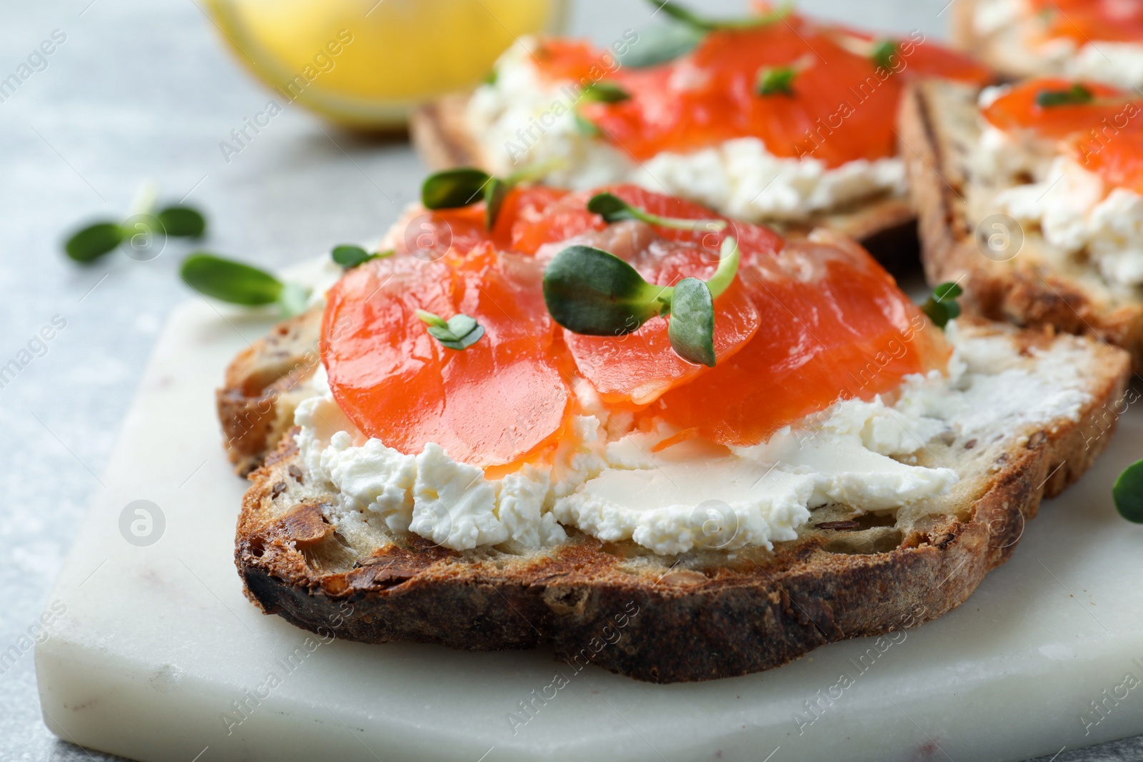 Photo of Delicious sandwich with cream cheese, salmon and microgreens on white marble board, closeup