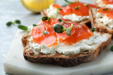 Delicious sandwich with cream cheese, salmon and microgreens on white marble board, closeup