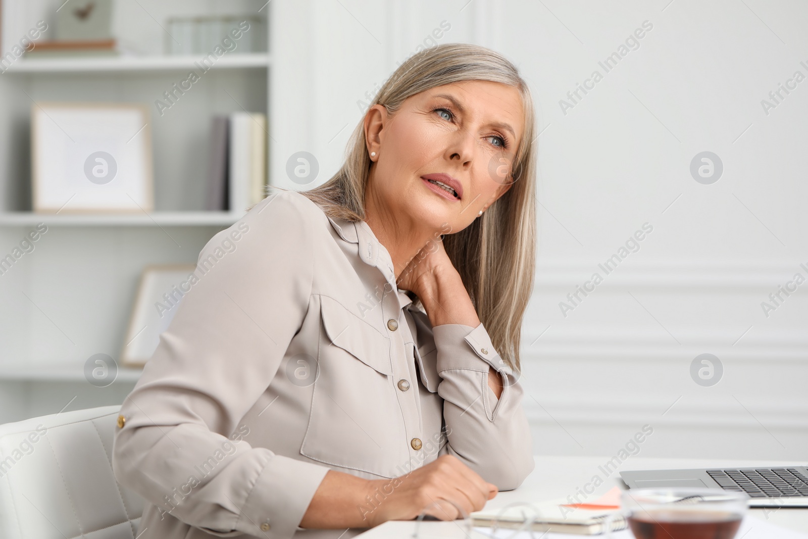 Photo of Woman suffering from neck pain at workplace in room