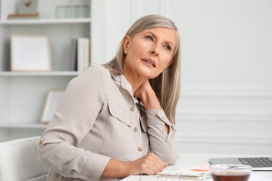 Woman suffering from neck pain at workplace in room