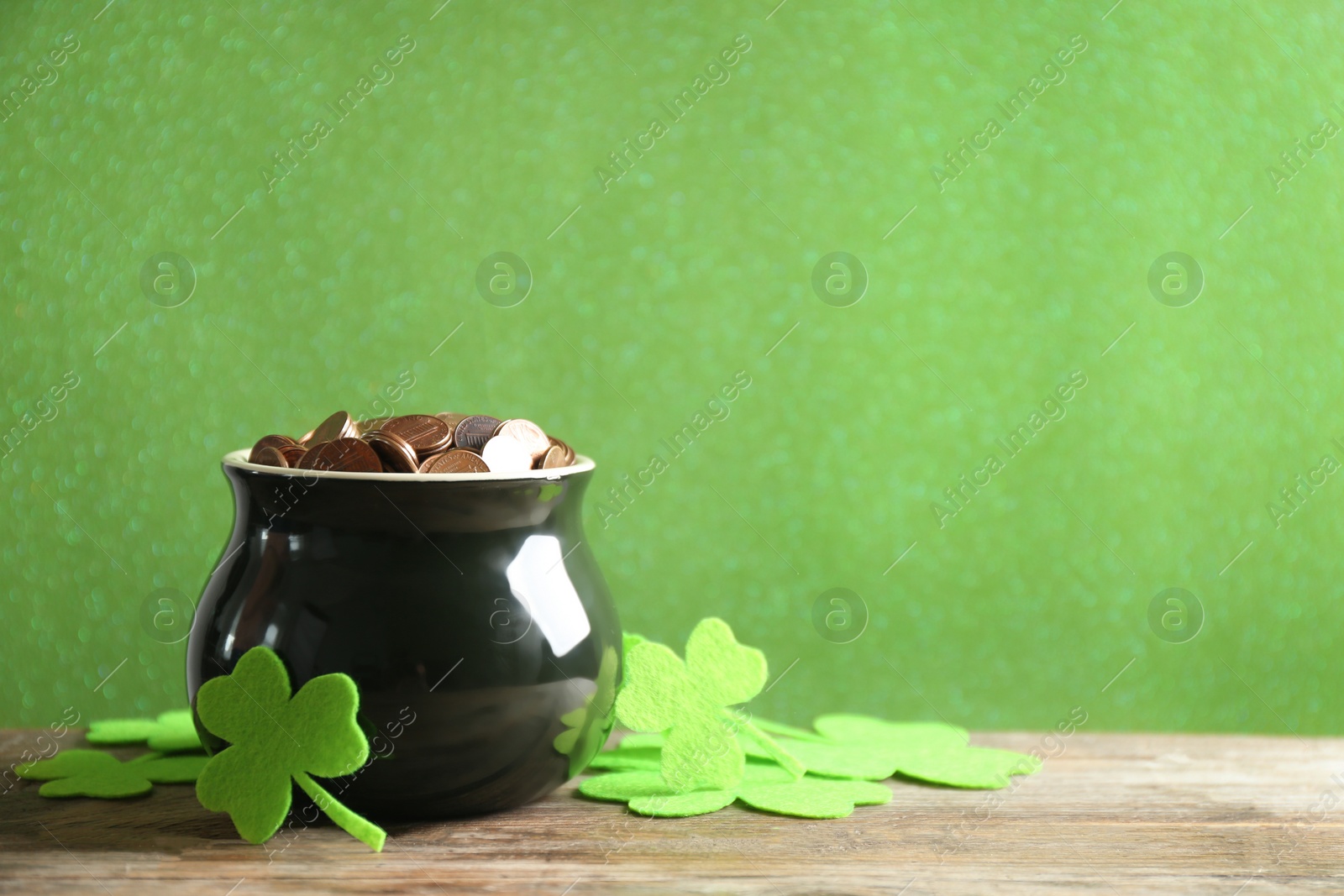 Photo of Pot of gold coins and clover leaves on wooden table against green background, space for text. St. Patrick's Day celebration