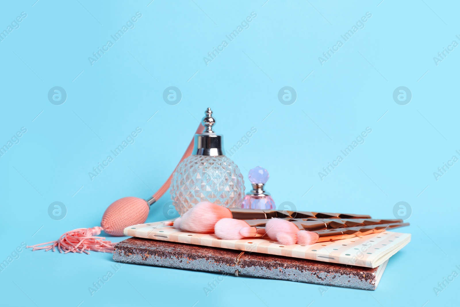 Photo of Composition with coral notebooks, brushes and perfume bottles on light blue background