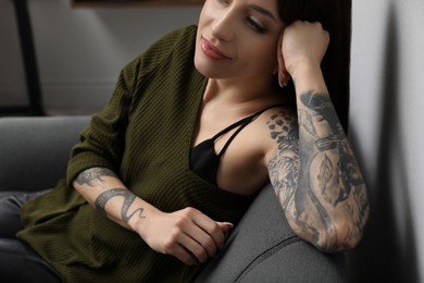 Photo of Beautiful woman with tattoos on arms resting in living room, closeup