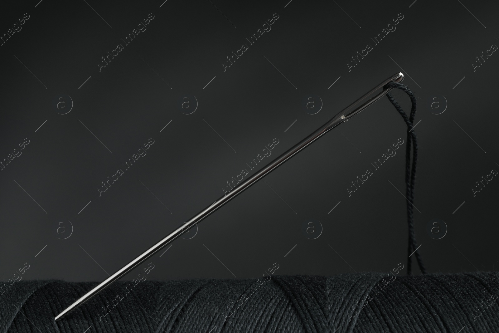 Photo of Black sewing thread with needle on grey background, closeup