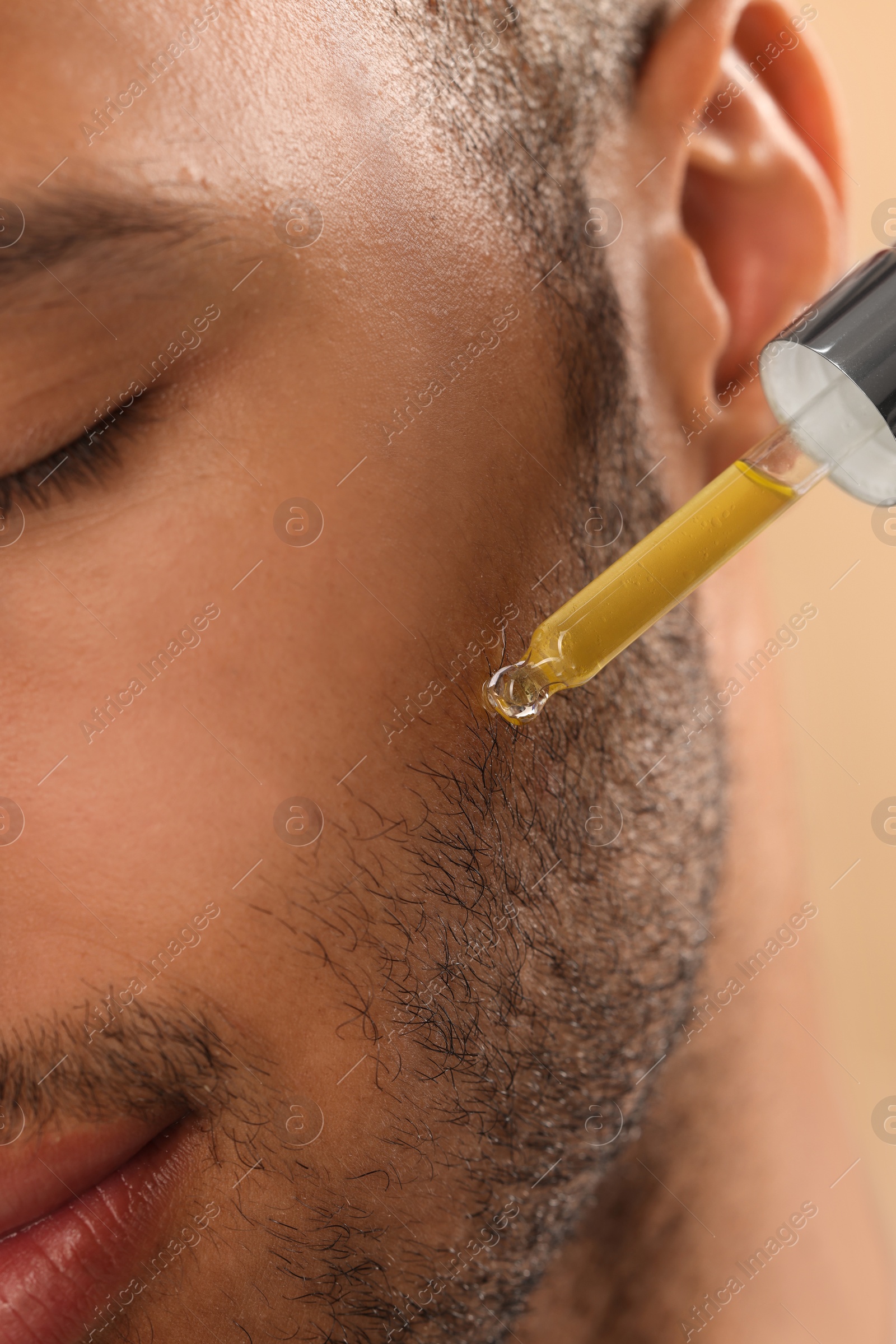 Photo of Man applying cosmetic serum onto face, closeup