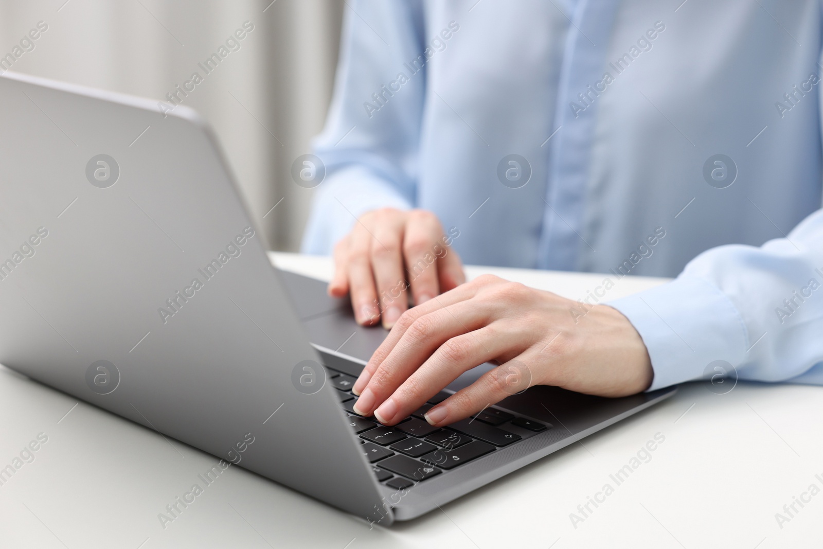 Photo of E-learning. Woman using laptop at white table indoors, closeup