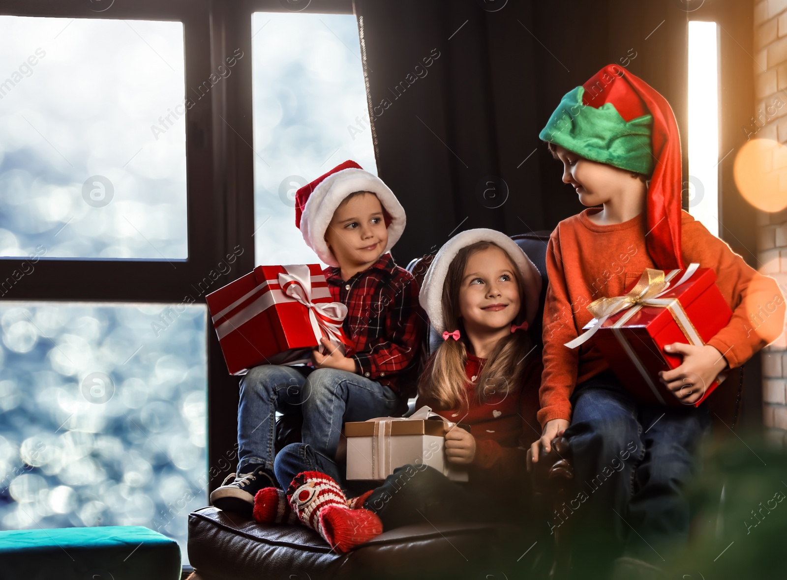 Photo of Little children with Christmas gifts near window indoors. Presents from Santa Claus