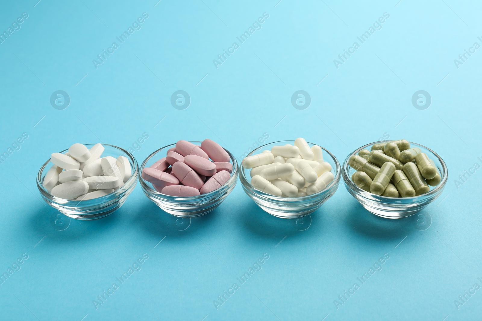 Photo of Different vitamin pills in bowls on light blue background