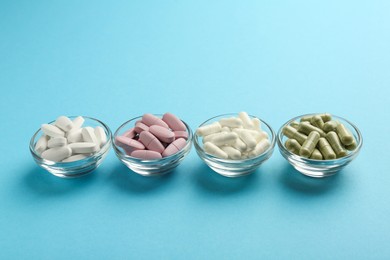 Different vitamin pills in bowls on light blue background