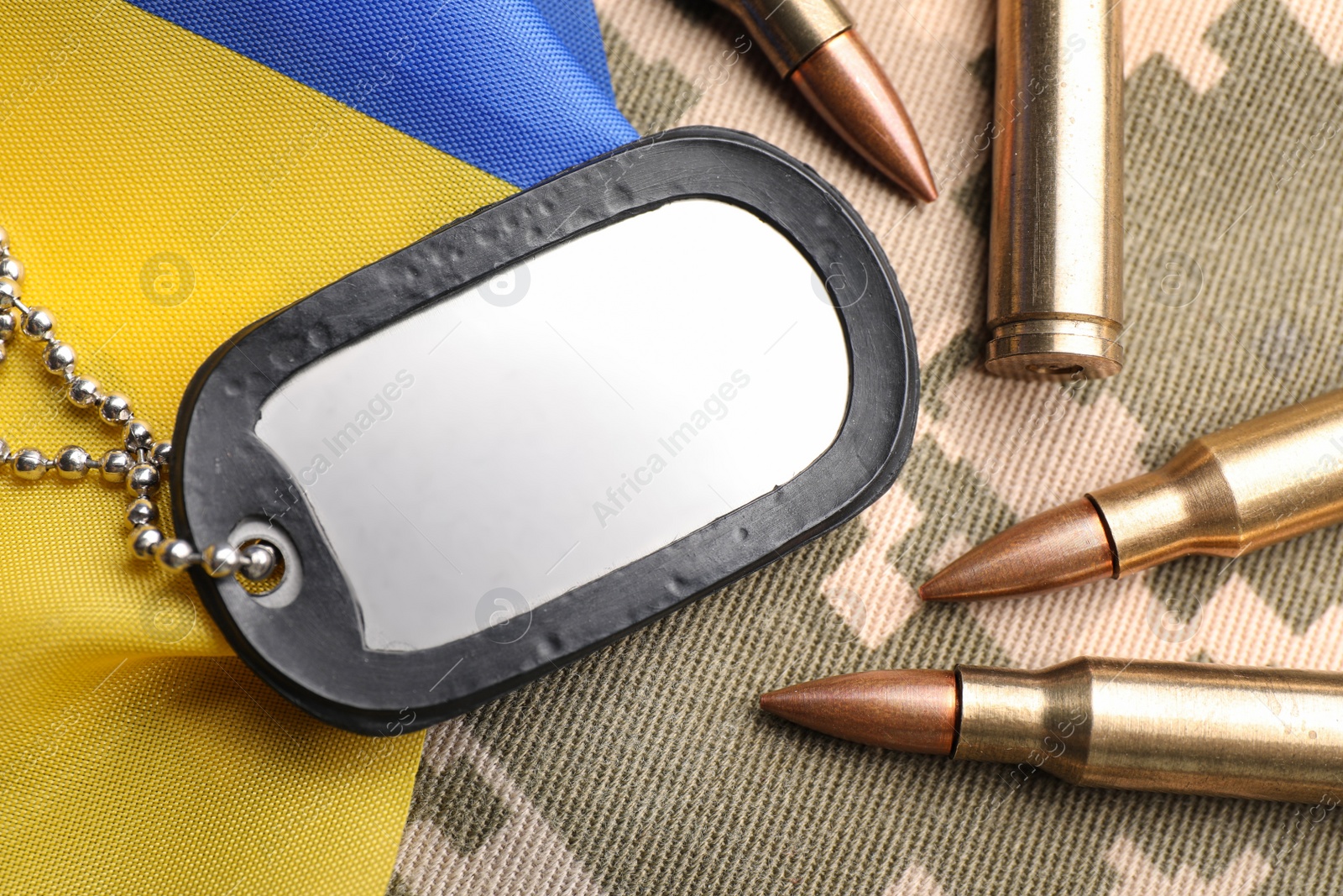 Photo of Military ID tag, bullets and Ukrainian flag on pixel camouflage, flat lay