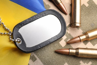 Military ID tag, bullets and Ukrainian flag on pixel camouflage, flat lay