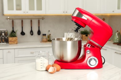 Photo of Modern red stand mixer, eggs and container with flour on white marble table in kitchen