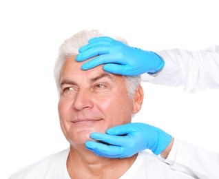 Photo of Doctor examining senior man face before cosmetic surgery on white background