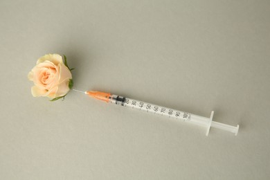 Photo of Medical syringe and beautiful rose on grey background, above view