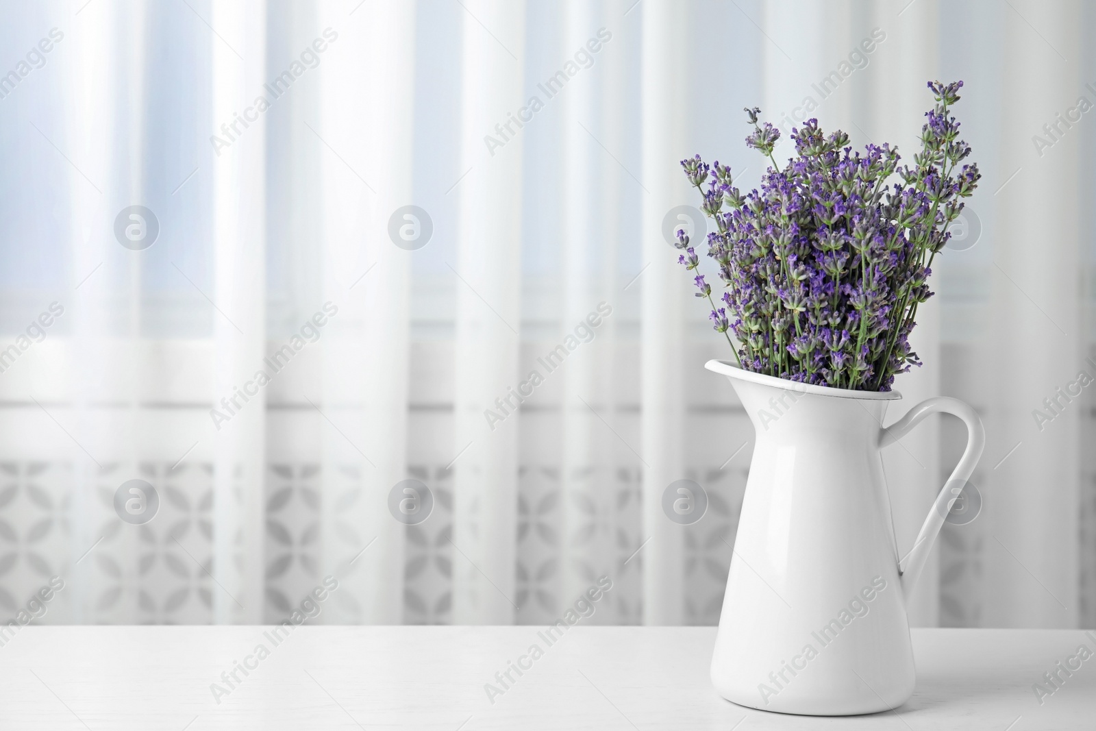 Photo of Beautiful tender lavender flowers in jug on white table indoors, space for text