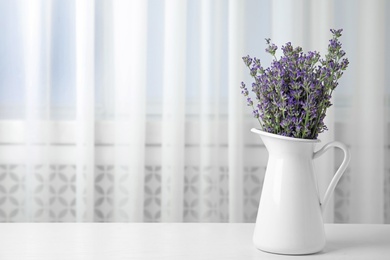 Photo of Beautiful tender lavender flowers in jug on white table indoors, space for text