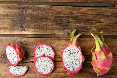 Delicious cut and whole dragon fruits (pitahaya) on wooden table, flat lay. Space for text