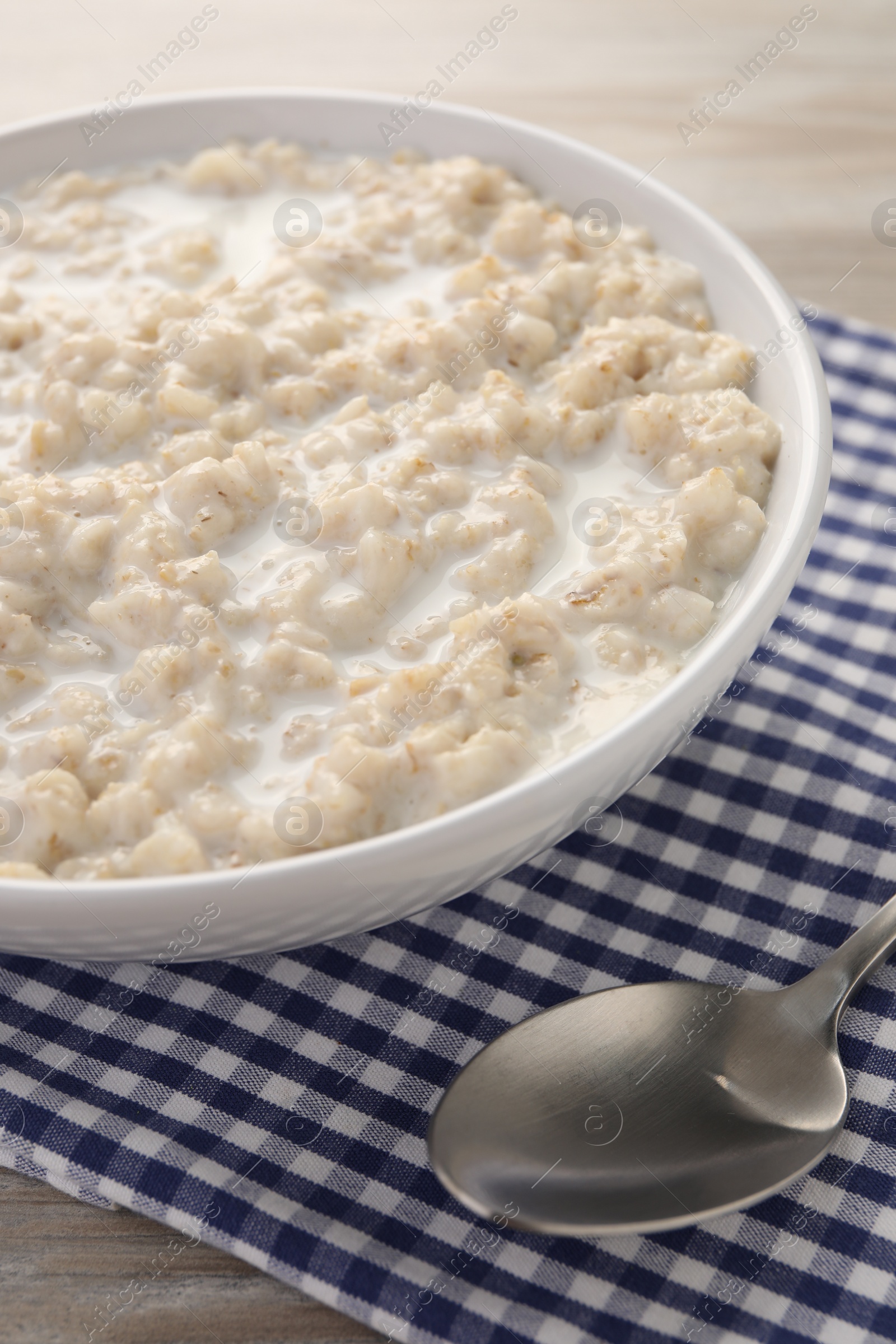 Photo of Tasty boiled oatmeal in bowl and spoon on table, closeup