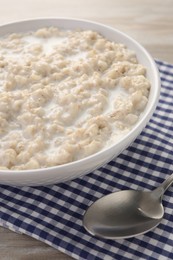 Tasty boiled oatmeal in bowl and spoon on table, closeup