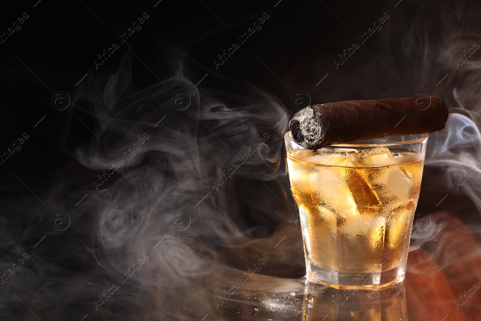 Photo of Glass of whiskey with ice cubes and smoldering cigar on black background. Space for text