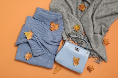 Photo of Flat lay composition with sweater and dry leaves on orange background. Autumn season