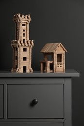 Photo of Wooden tower and house on chest of drawers near dark grey wall. Children's toys